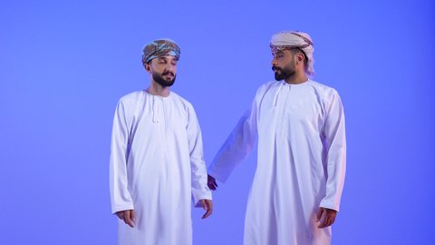 ايماءات تدل على الموافقة والقبول، بورتريه لرجلان عربيان خليجيان عمانيان يرتدي الدشداشة و العمامه يقومان بالاشارة باصبع الابهام للاعلى تظهر عليهم تعابير الفرح والسرور، الرضى وعدم الرفض, خلفية زرقاء