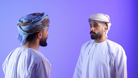 تبادل الأفكار وبناء علاقات اجتماعية, بورترية لصديقان عربيان خليجيان عمانيان يرتديان الدشداشة و العمامة يستمتعان بتبادل االاحاديث، نقاشات وحوارات، قضاء اوقات ممتعة، وناسة وتعارف، خلفية زرقاء