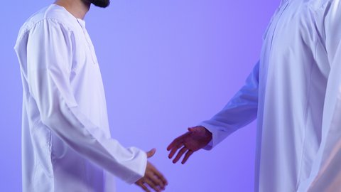 مفهوم الصفح والتسامح، إلقاء السلام والتحية, بورترية مقرب ليد لرجلين عربيين خليجيين عمانيين يرتديان الزي التقليدي يتصافحان سوياً, بناء العلاقات الاجتماعية المتينة في المجتمع العماني، خلفية زرقاء