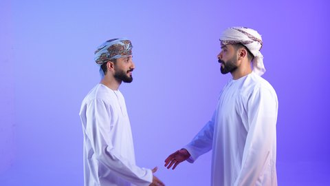 إلقاء السلام والتحية, مفهوم الصفح والتسامح, بورترية لرجلين عربيين خليجيين عمانيين يرتديان الدشداشة و العمامة  يتصافحان سوياً, بناء العلاقات الاجتماعية المتينة في المجتمع العماني، خلفية زرقاء