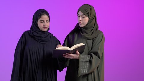 Spending free time learning and culture, hobby of reading and exploration, concept of education and scientific research, portrait of a Saudi Arabian Gulf woman wearing an abaya and hijab holding a book in her hand with her friend, scientific books and cultural novels, colorful background