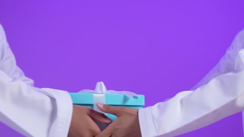 أعياد ومناسبات ومفاجآت سعيدة، مشاركة وتقديم الهدايا في الأعياد والمناسبات السعيدة، التعبير عن المحبة والألفة بين الاصدقاء, بورتريه مقرب ليد لطفل عربي خليجي عماني يرتدي الزي التقليدي  يقوم بتقديم الهدية لتوأمة, خلفية بنفسجية