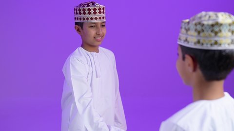 إلقاء السلام والتحية, مفهوم الصفح والتسامح, بورترية لطفلان  توأمان عربيان خليجيان عمانيان يرتديان الدشداشة و الكمه يتصافحان سوياً, بناء العلاقات الاجتماعية المتينة في المجتمع العماني ، خلفية بنفسجية