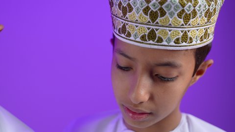 تصفح التطبيقات والبرامج الالكترونية عبر الابتوب، استخدام الأجهزة التقنية الحديثة والمتطورة، بورترية مقرب لطفل عربي خليجي عماني يرتدي الدشداشة و الكمه يقوم ببتصفح الانترنت من خلال الحاسب المحمول برفقة توأمه بايماءات السعادة و السرور، خلفية ينفسجية