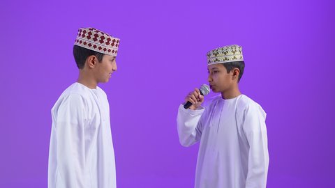 تقديم العروضات المسرحية، ايماءات وجه و يدين تدل على السعادة و الاستمتاع ، بورترية لطفل عربي خليجي عماني يرتدي الدشداشة و الكمه يحمل بيده الميكروفون برفقه توأمه، موهبة الغناء ، خلفية بنفسجية
