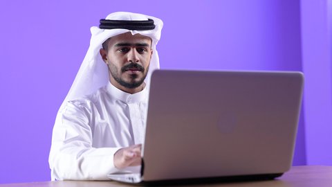 موظف سعودي يستخدم التقنيات الحديثة في الأعمال الإدارية والمكتبية ، التوظيف في المكاتب والشركات الكويتية، التركيز والتفاني والعمل الجاد، رجل عربي خليجي كويتي يرتدي الثوب التقليدي والغترة يجلس على مكتب ويعمل على جهاز الحاسب المحمول