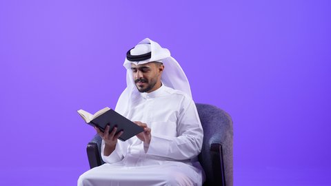 الاستمتاع بالأنشطة الترفيهية المفيدة في وقت الفراغ, مفهوم الثقافة والتعلم الذاتي, قراءة القصص والروايات, شاب عربي خليجي كويتي يرتدي الثوب التقليدي يجلس على كرسي مريح يحمل كتاب وينظر اليه بايماءات الاندماج ، رجل سعودي يمارس هواية المطالعة