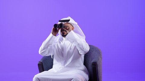 رؤية الأشياء البعيدة وتقريبها, إيماءات الاستمتاع والسرور, شاب سعودي يحب الاستكشاف و المغامرة, رجل عربي خليجي كويتي يرتدي الثوب التقليدي يجلس على كرسي مريح ينظر من خلال منظار ثنائي العينين يشير بإصبع السبابة إلى شيئ ما