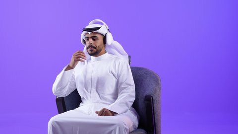 الاندماج و التفاعل مع الانغام الموسيقية، مواهب غنائية فنية، شاب عربي خليجي كويتي يرتدي الثوب التقليدي والغتره يجلس على كرسي مريح يستمع الى الموسيقى من خلال سماعه الرأس، رجل سعودي ينصت ويستمع للأغاني بإستخدام الهيدفون
