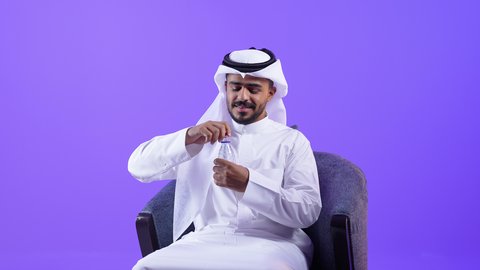 The importance of drinking pure water to maintain healthy skin. A young Kuwaiti Gulf Arab man wearing a traditional shemagh and thobe drinks water from a plastic bottle. A Saudi man maintains a healthy immune system and detoxifies the body.