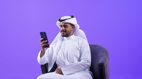 التقاط الصور التذكارية ، تصفح مواقع وتطبيقات الانترنت، الدردشة والتحدث مع الأصدقاء، شاب عربي خليجي كويتي مبتسم يرتدي الثوب التقليدي والغتره يمسك الجوال بيده، رجل سعودي يستخدم التقنيات والتكنولوجيا الحديثة بالحياة اليومية