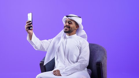 توثيق اللحظات التذكارية عبر السيلفي، تصفح مواقع وتطبيقات الانترنت، الدردشة والتحدث مع الأصدقاء، شاب عربي خليجي كويتي مبتسم يرتدي الثوب التقليدي والغتره يمسك الجوال بيده، رجل سعودي يستخدم التقنيات والتكنولوجيا الحديثة بالحياة اليومية