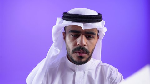 الاستمتاع بالأنشطة الترفيهية المفيدة في وقت الفراغ,  مفهوم الثقافة والتعلم الذاتي, قراءة القصص والروايات,تصوير مقرب لشاب عربي خليجي كويتي يرتدي الثوب التقليدي يجلس على كرسي مريح يحمل كتاب وينظر اليه بايماءات الاندماج ، رجل سعودي يمارس هواية المطالعة