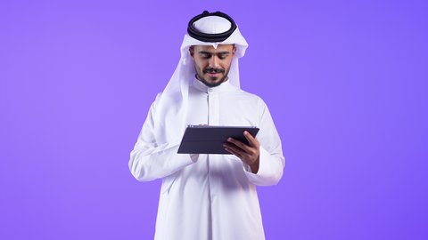 استخدام الأجهزة والتقنيات الحديثة المتطورة، اجتماع عمل عبر الإنترنت، رجل عربي خليجي كويتي يرتدي الثوب التقليدي يجلس على كرسي مريح يقوم بإجراء مكالمة فيديو عبر جهاز التابلت ، رجل سعودي يدير شؤون الأعمال وينظمها عن بعد