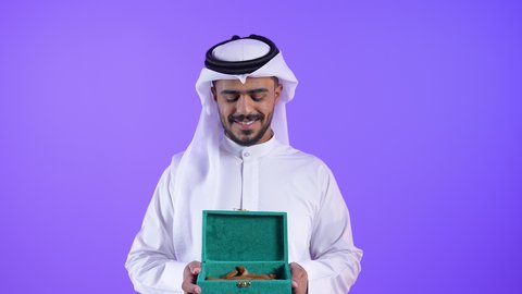 التسويق لمنتجات العود والبخور, رجل عربي كويتي خليجي يرتدي الثوب التقليدي والغترة يحمل بيده صندوق مليء بخشب العود الفاخر، التبخر والتعطر بخشب العود العطري، مناسبات الأعياد والحفلات، منتج محلي كويتي ، شاب سعودي يحمل علبة بخور خشبي