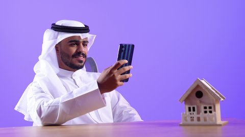 تصفح مواقع وتطبيقات الانترنت، النظر إلى الهاتف المحمول بإيماءات الاندماج، الدردشة والتحدث مع الأصدقاء، شاب عربي خليجي كويتي مبتسم يرتدي الثوب التقليدي والغتره يمسك الجوال بيده، رجل سعودي يستخدم التقنيات والتكنولوجيا الحديثة بالحياة اليومية