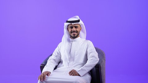 تعابير السعادة والسرور، رجل عربي خليجي كويتي مبتسم يرتدي الثوب التقليدي والغترة يجلس على كرسي ينظر الى الكاميرا بإيماءات الفرح والثقة بالنفس ، رجل سعودي مهتم بالاناقة والاهتمام بالمظهر الخارجي