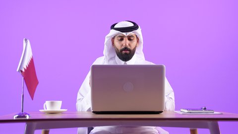 العمل في المكاتب والشركات القطرية، اجراء مكالمة فيديو، دمج التقنيات الحديثة بالمجال الإداري، الاستمتاع بتناول فنجان من القهوة الساخنة، بورتريه لرجل عربي خليجي قطري يرتدي الثوب التقليدي والغترة يجلس خلف طاولة المكتب وبجانبه علم قطر يعمل على الحاسوب المحمول، خلفية بنفسجية