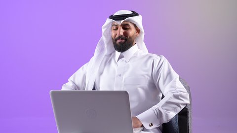 ايماءات الترحيب والتحية والسلام، دمج التقنيات الحديثة في الحياة اليومية،رجل سعودي يقوم بالتواصل مع الاهل والاصدقاء عبر الانترنت, بورتريه لرجل عربي خليجي قطري يرتدي الثوب التقليدي والغترة يجلس على كرسي مريح يقوم بإجراء مكالمة فيديو عبر جهاز اللابتوب، خلفية بنفسجية