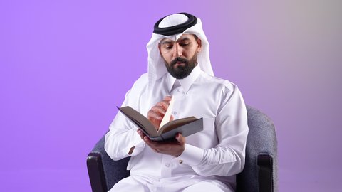 الاستمتاع بقراءة الكتب والقصص والروايات، تنمية المهارات وتوسيع المعارف والأفكار، بورتريه لرجل عربي خليجي قطري يرتدي الثوب التقليدي والغترة يجلس على كرسي ويمسك بيديه كتاب، زيادة الذخيرة الفكرية، شاب سعودي يقوم بقضاء أوقات الفراغ بشكل مفيد، خلفية بنفسجية