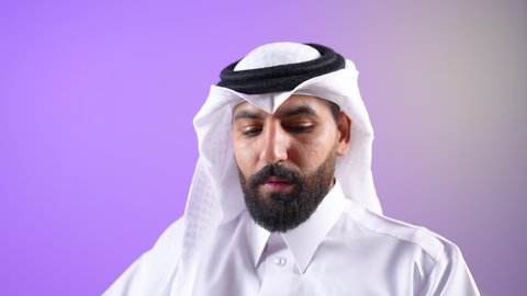 Developing skills and expanding knowledge and ideas, enjoying reading books, stories and novels, close-up portrait of a Qatari Gulf Arab man wearing traditional thobe and ghutra sitting on a chair and holding a book in his hands, increasing intellectual reserve, a Saudi young man spending his free time in a useful way, purple background