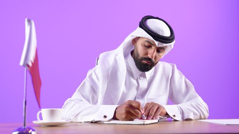Luxury business companies in Qatar, office management jobs and professions, close-up portrait of a Qatari Gulf Arab man wearing traditional thobe and ghutra sitting behind a desk writing and following up on his work with gestures and expressions of seriousness and self-confidence, purple background