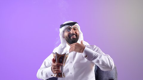 اتباع العادات والتقاليد العربية الأصيلة، شاب سعودي يقوم بالتبخير واستخدام العطور والمطيبات، التبخر في الأعياد والمناسبات السعيدة، بورتريه  لرجل عربي خليجي قطري يرتدي الثوب التقليدي والغترة يجلس على كرسي ويمسك بيده المبخرة، خلفية بنفسجية