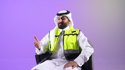 مفهوم الهندسة والانشاءات المعمارية, شاب سعودي يعمل في القطاع الهندسي، بورتريه لرجل عربي خليجي قطري يرتدي الثوب مع سترة الحماية والغترة يجلس على كرسي مريح يشير بيديه الى شيء ما، إدارة ومتابعة المشروع, خلفية بنفسجية