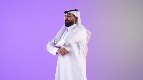 مفهوم الرجولة والقوة والثقة بالنفس، الاهتمام بالأناقة والمظهر الخارجي، شاب سعودي النظر إلى الكاميرا بايماءات الجدية والسرور، بورتريه لرجل عربي خليجي قطري يرتدي الثوب التقليدي والغترة يقف بأيدي متقاطعة بتعابير الحزم، خلفية بنفسجية