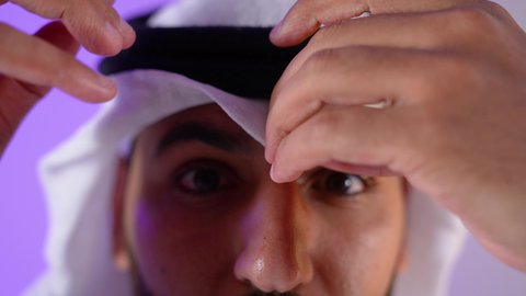 الاهتمام بالأناقة والمظهر الخارجي، شاب سعودي النظر إلى الكاميرا بايماءات الجدية والسرور، مفهوم الرجولة والقوة والثقة بالنفس، بورتريه مقرب لرجل عربي خليجي قطري يرتدي الثوب التقليدي والغترة يقف بأيدي متقاطعة بتعابير الحزم، خلفية بنفسجية