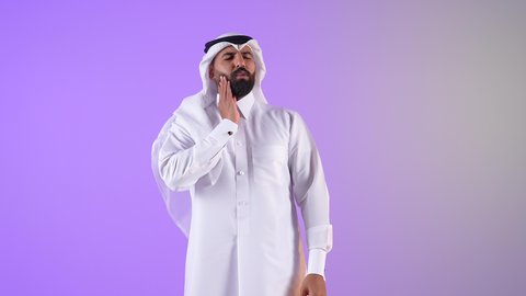 مشاكل التهاب اللثة وتسوس الأسنان, شاب سعودي يشيرإلى الفم بتعابير الإرهاق والتعب, بورتريه لرجل عربي خليجي قطري يرتدي الثوب التقليدي والغتره يضع يده على فمه بإيماءات الانزعاج والألم الشديد، خلفية بنفسجية