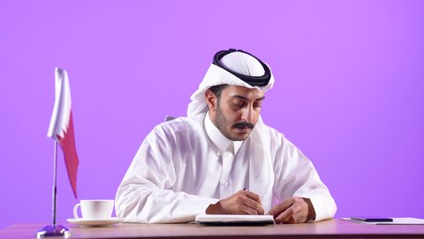 مهن ووظائف ادارية مكتبية، بورتريه مقرب لرجل عربي خليجي قطري يرتدي الثوب التقليدي والغترة يجلس خلف المكتب يكتب و يتابع اعماله بايماءات وتعابير الجدية والثقة بالنفس، شركات الأعمال الفاخرة في قطر، خلفية بنفسجية