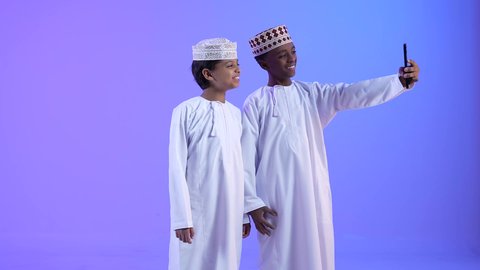 التقاط الصور التذكارية، صديقان عربيان خليجيان عمانيان يرتديان الدشداشة والكمة بايماءات وجه ويدين تدل على السعادة، استخدام الهاتف المحمول،  توثيق اللحظات السعيدة، اجراء مكالمة فيديو