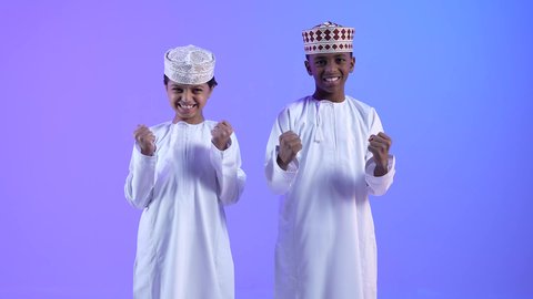 علامات وتعابير والفرح والقوة ، الإعجاب والرضا و الشعور بالسعاده، تحقيق الاهداف و إنجاز المهام, صديقان عربيان خليجيان عمانيان يرتديان الدشداشة والكمة ، يرفعان قبضة اليد بإيماءات النصر والفوز و الكسب