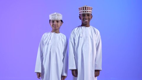 الاهتمام بالأناقة والمظهر الخارجي، مشاعر الحب بين الاخوة,  صديقان عربيان خليجيان عمانيان يرتديان الدشداشة والكمة ، ينظران الى الكاميرا بإيماءات السرور، التقاط الصور الشخصية