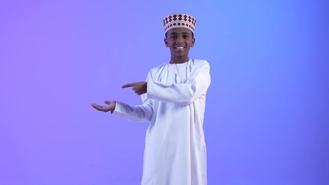 التوضيح والاشارة إلى شيء ما، ولد عربي عماني خليجي يرتدي الدشداشة والكمة ويشير بيده إلى مكان ما، تحديد موقع معين بايماءات السعادة والسرور، إشارات وحركات يدين تدل على هذا المكان (هنا)