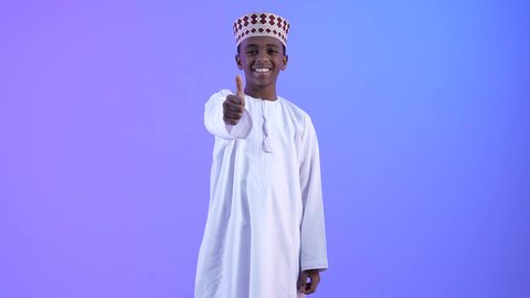 تعابير الإعجاب والرضى، ولد عربي خليجي عماني مبتسمة يرتدي الدشداشة والكمة يرفع اصبع الابهام بإيماءات الامتياز والجودة، مفهوم القبول والموافقه