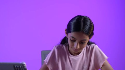 مراجعة الدروس اليومية عبر الانترنت، تلقي المحاضرات المدرسيه عن بعد، تطور العلم والتعليم في سلطنه عمان، طالبة عربية خليجية عمانية ترتدي الزي الكاجوال تجلس على طاولة امام جهاز التابلت المحمول تقوم بحل الواجبات المدرسيه