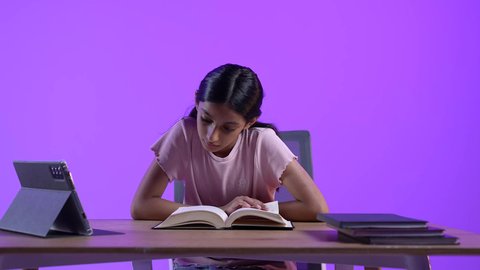 طالبة عربية خليجية عمانية ترتدي الزي الكاجوال تجلس على طاولة امام جهاز التابلت المحمول تقوم بحل الواجبات المدرسيه ، مراجعة الدروس اليومية عبر الانترنت، تلقي المحاضرات المدرسيه عن بعد، تطور العلم والتعليم في سلطنه عمان