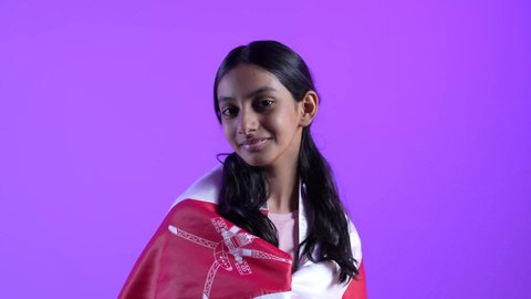 Commemorating Oman's National Day, a close-up of an Omani Gulf Arab girl wearing casual clothes and the flag of the Sultanate of Oman with gestures of joy and happiness, pride in Omani symbols, the concept of love of the homeland and belonging to it