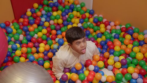 Fun and entertainment times, a Saudi child with Down syndrome at an amusement park, playing in a plastic ball pool, gestures of pleasure and happiness, having a wonderful time at the amusement park, enjoying summer vacation.