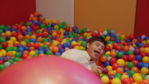 ايماءات السرور والسعادة، قضاء اوقات رائعة في مدينة الملاهي ،  الاستمتاع باللعب في العطلة الصيفية ، اوقات التسلية و الترفيه ،طفل سعودي مصاب بمتلازمة داون في مدينة الألعاب ، يلعب في حوض الكور البلاستيكية