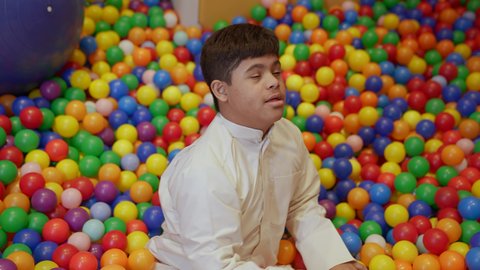 الاستمتاع باللعب في العطلة الصيفية ، اوقات التسلية و الترفيه ،قضاء اوقات رائعة في مدينة الملاهي ، طفل سعودي مصاب بمتلازمة داون في مدينة الألعاب ، يلعب في حوض الكور البلاستيكية