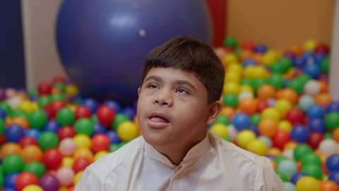 Fun and entertainment times, enjoying summer vacation, having a great time at an amusement park, a Saudi child with Down syndrome at an amusement park, playing in a plastic ball pool.