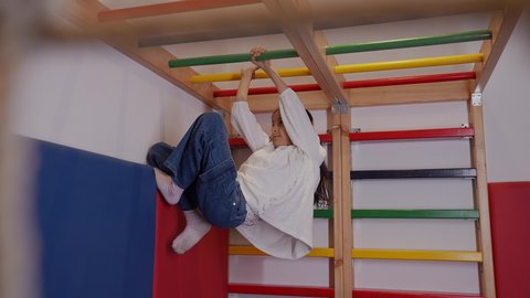 مفهوم ممارسة الأنشطة الحركية للأطفال، فتاة عربية خليجية سعودية ترتدي الملابس الكاجوال، تقوم بالتسلق واللعب على قضبان ملونة في صالة الألعاب المخصصة للأطفال، تعابير التركيز والمتعة، تنمية المهارات الجسدية وتعزيز النشاط البدني