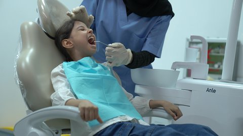 الاهتمام والرعاية الصحية، معالجة النخر والتسوس، المعدات اللازمة لإجراء الفحوصات، بنت عربية خليجية سعودية ترتدي الزي الكاجوال ، تجلس في العيادة السنية وتفتح فمها لتشخيص المرض ،طبيبة عربية خليجية سعودية ترتدي الكمامة والقفازات الطبية تقوم بفحص أسنان المريض