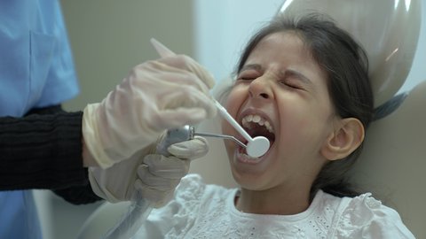 معالجة النخر والتسوس،  المعدات اللازمة لإجراء الفحوصات، طبيبة عربية خليجية سعودية ترتدي الكمامة والقفازات الطبية تقوم بفحص أسنان المريض ، بنت عربية خليجية سعودية ترتدي الزي الكاجوال ، تجلس في العيادة السنية وتفتح فمها لتشخيص المرض