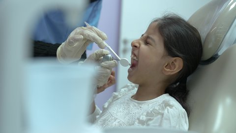 المعدات اللازمة لإجراء الفحوصات، طبيبة عربية خليجية سعودية ترتدي الكمامة والقفازات الطبية تقوم بفحص أسنان المريض ، بنت عربية خليجية سعودية ترتدي الزي الكاجوال ، تجلس في العيادة السنية وتفتح فمها لتشخيص المرض ،معالجة النخر والتسوس