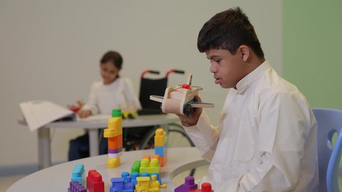 Spending fun time playing and concentrating, entertainment centers in Saudi Arabia, enhancing mental and intellectual skills, a Saudi boy with Down syndrome assembling blocks, caring for and developing children's skills.
