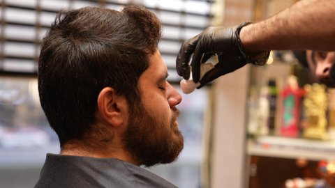 مفهوم العناية بالبشرة والنظافة، روتين العناية بالبشرة، تصوير مقرب ليد حلاق عربي خليجي سعودي يقوم بتنظيف البشرة للزبون، صالون رجالي تجميلي